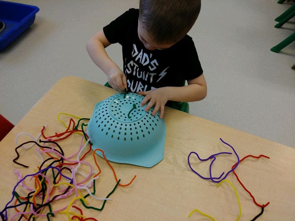 Child pushing pipe cleaners into a colander