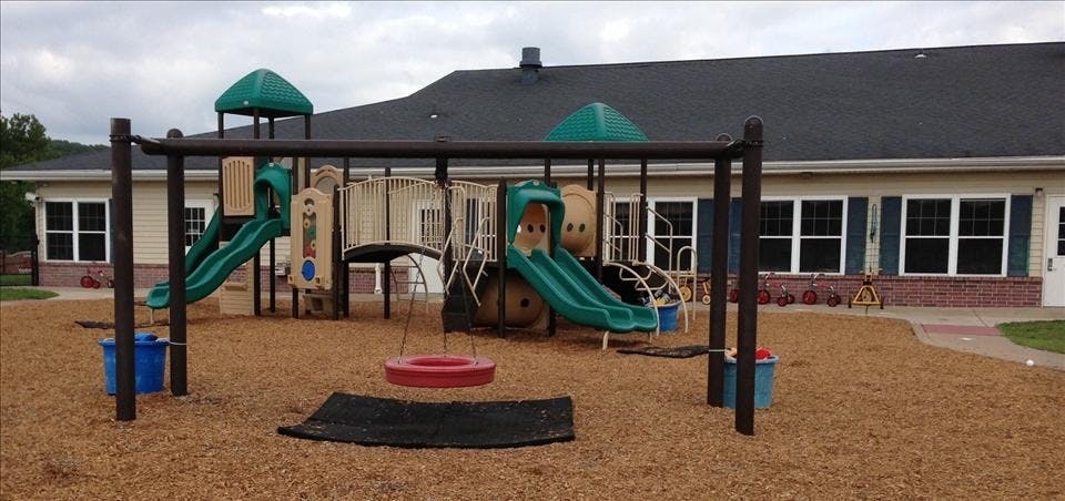 Playground with swings, slides, and climbing structures on wood chips, in front of a building