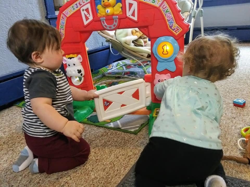 Two children playing with a red toy barn