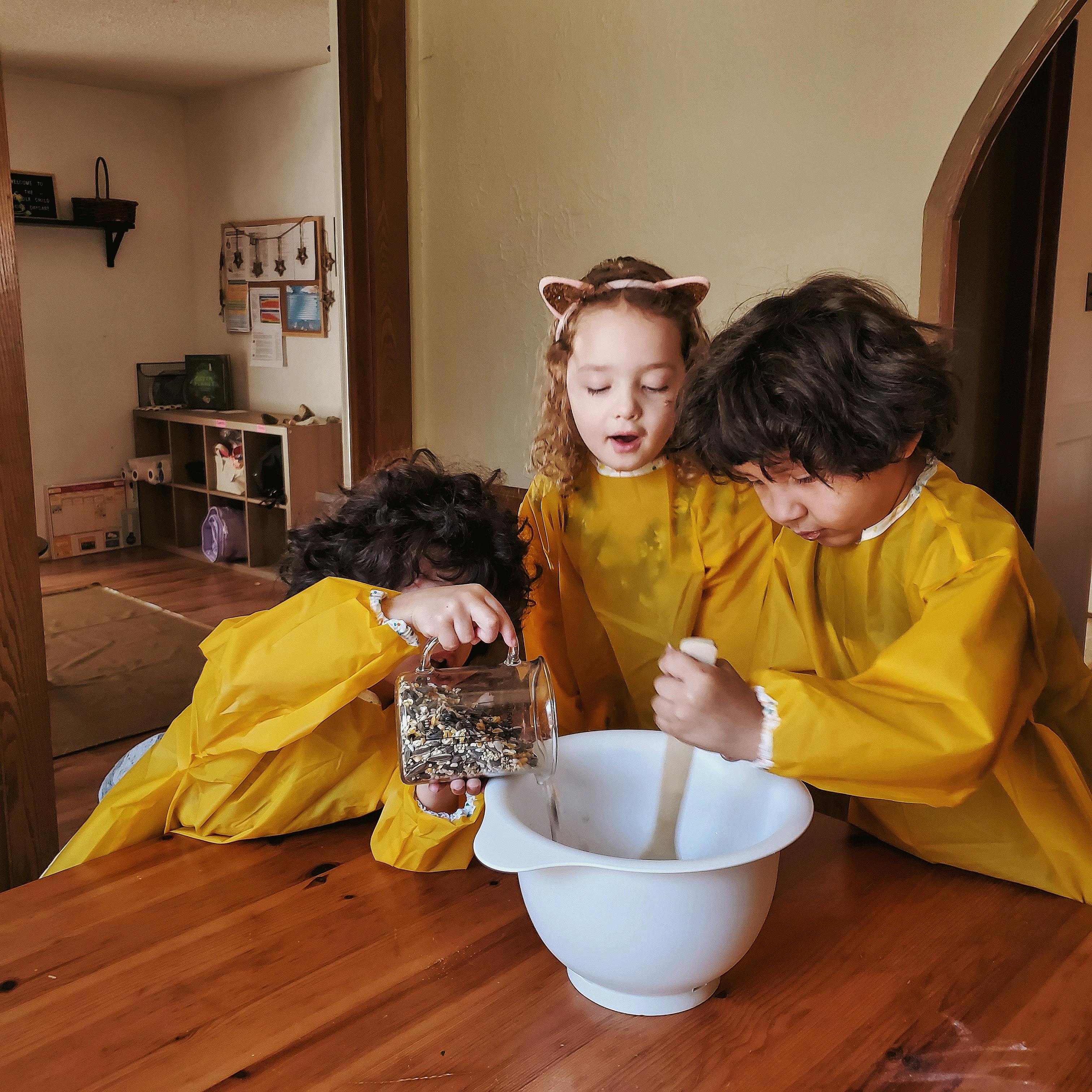 Three children in yellow smocks preparing food in a bowl