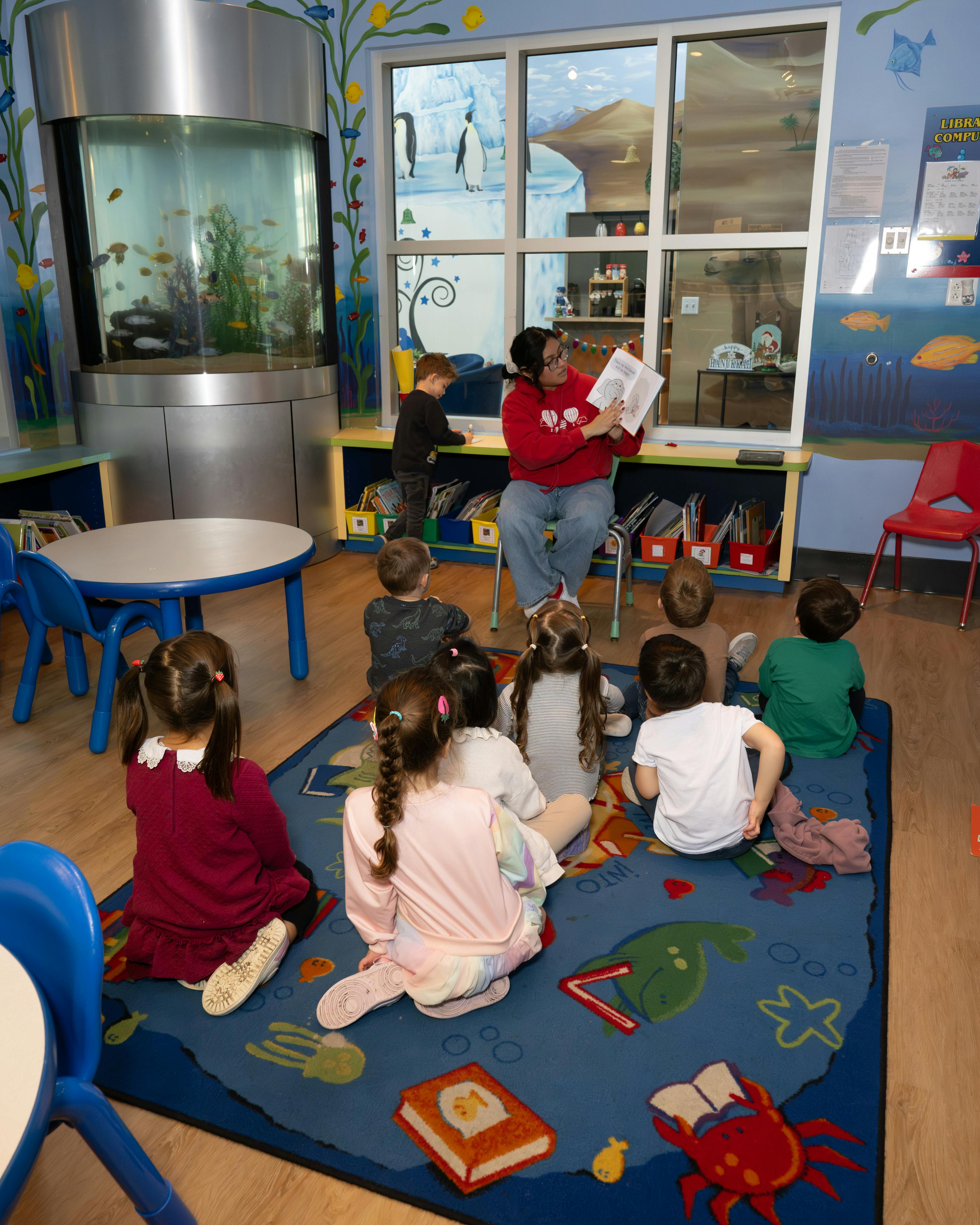Person reading a book to a group of children sitting on a rug