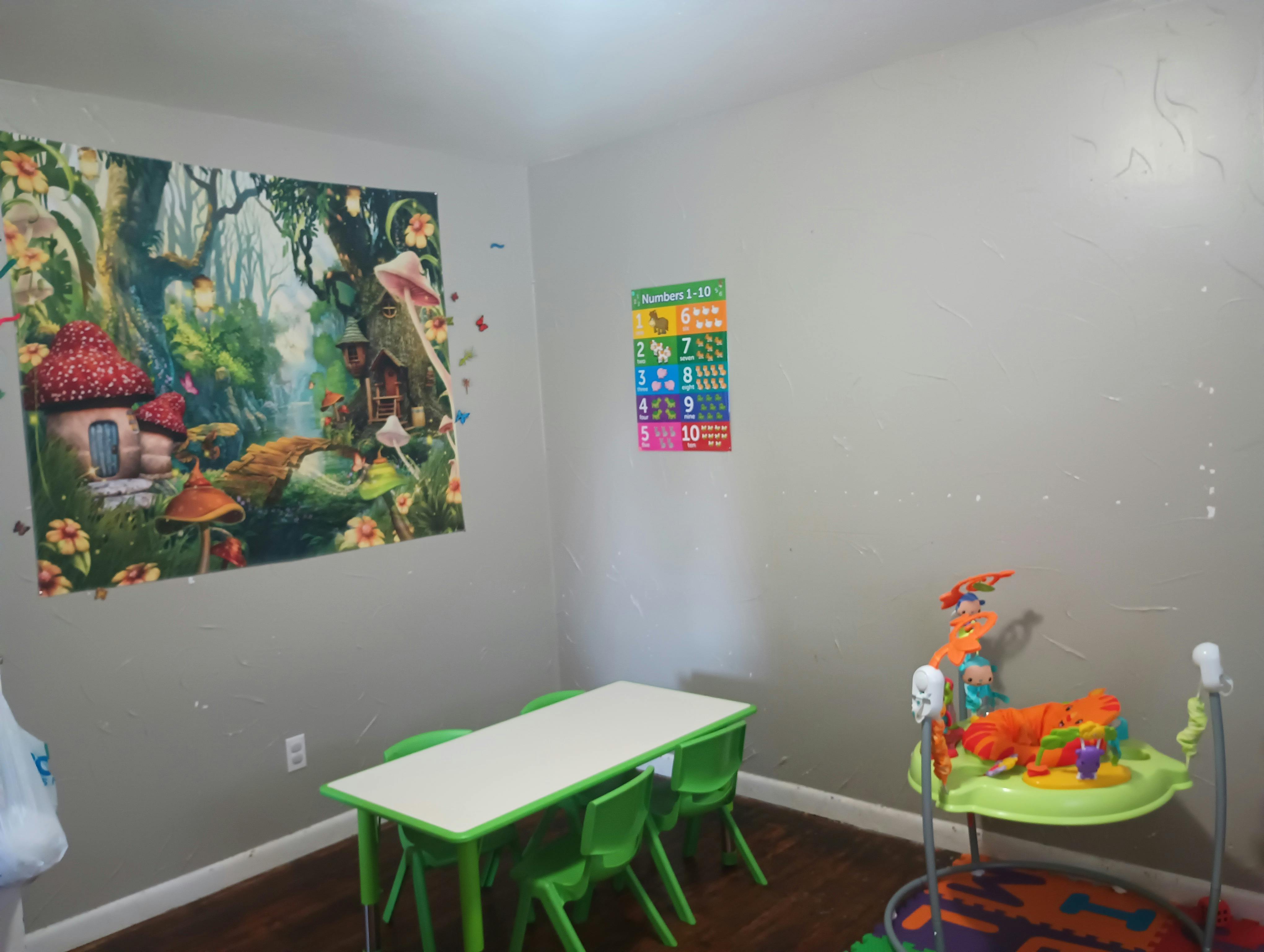 Children's room with a table and chairs, wall mural, and baby activity center