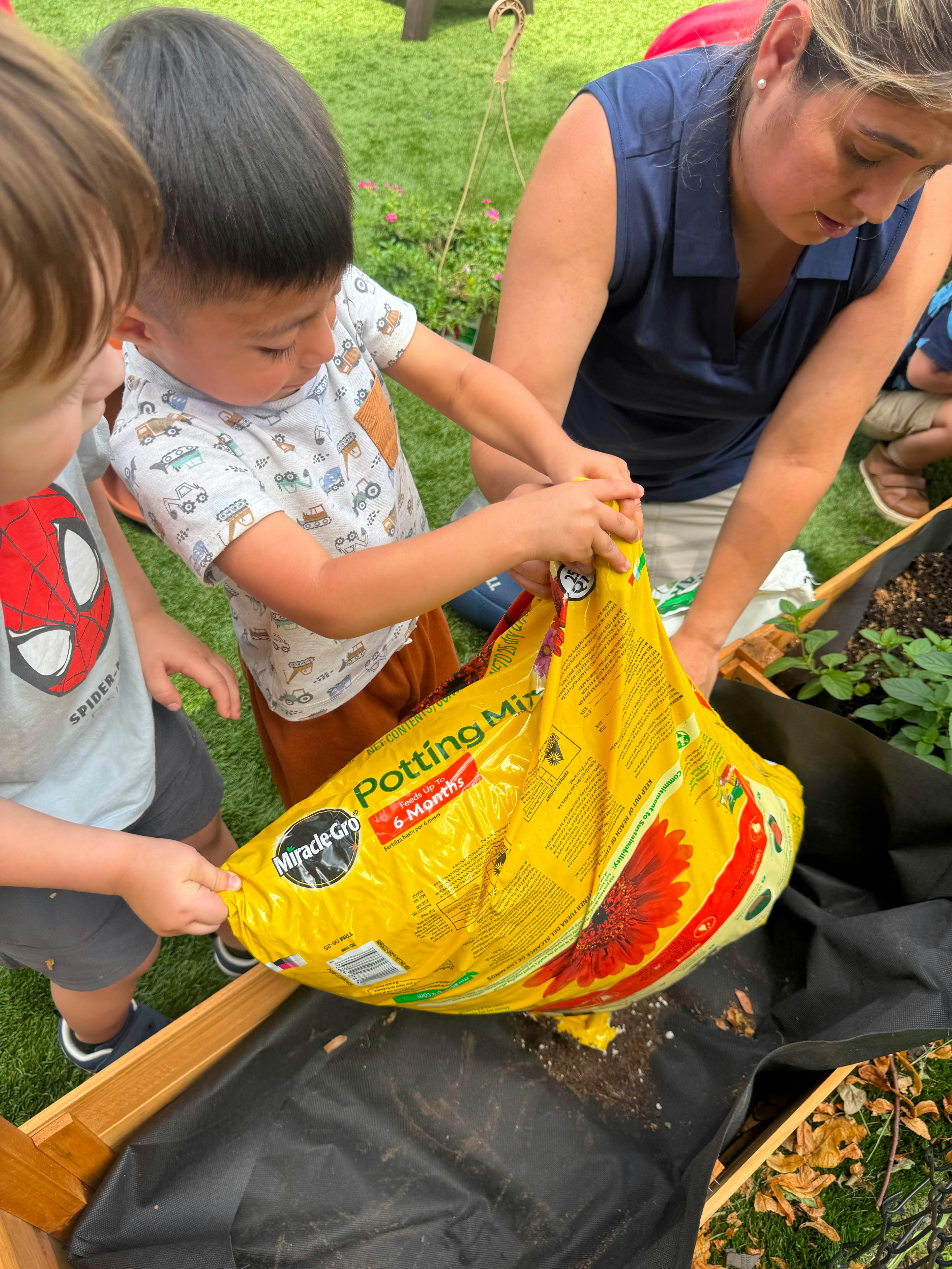 Adult and two children pouring potting mix into a wooden garden bed