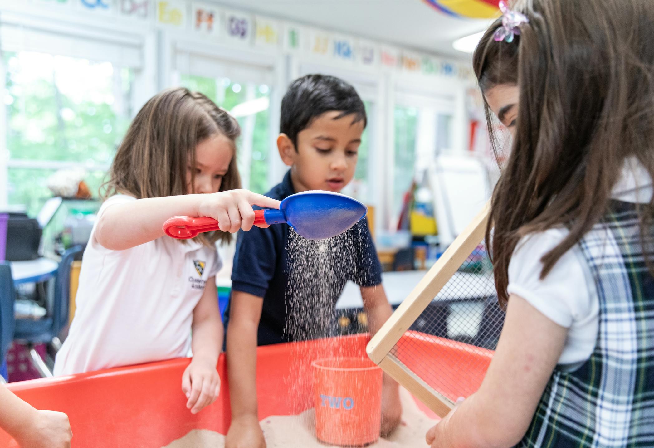Three children playing with sand and toys in a classroom