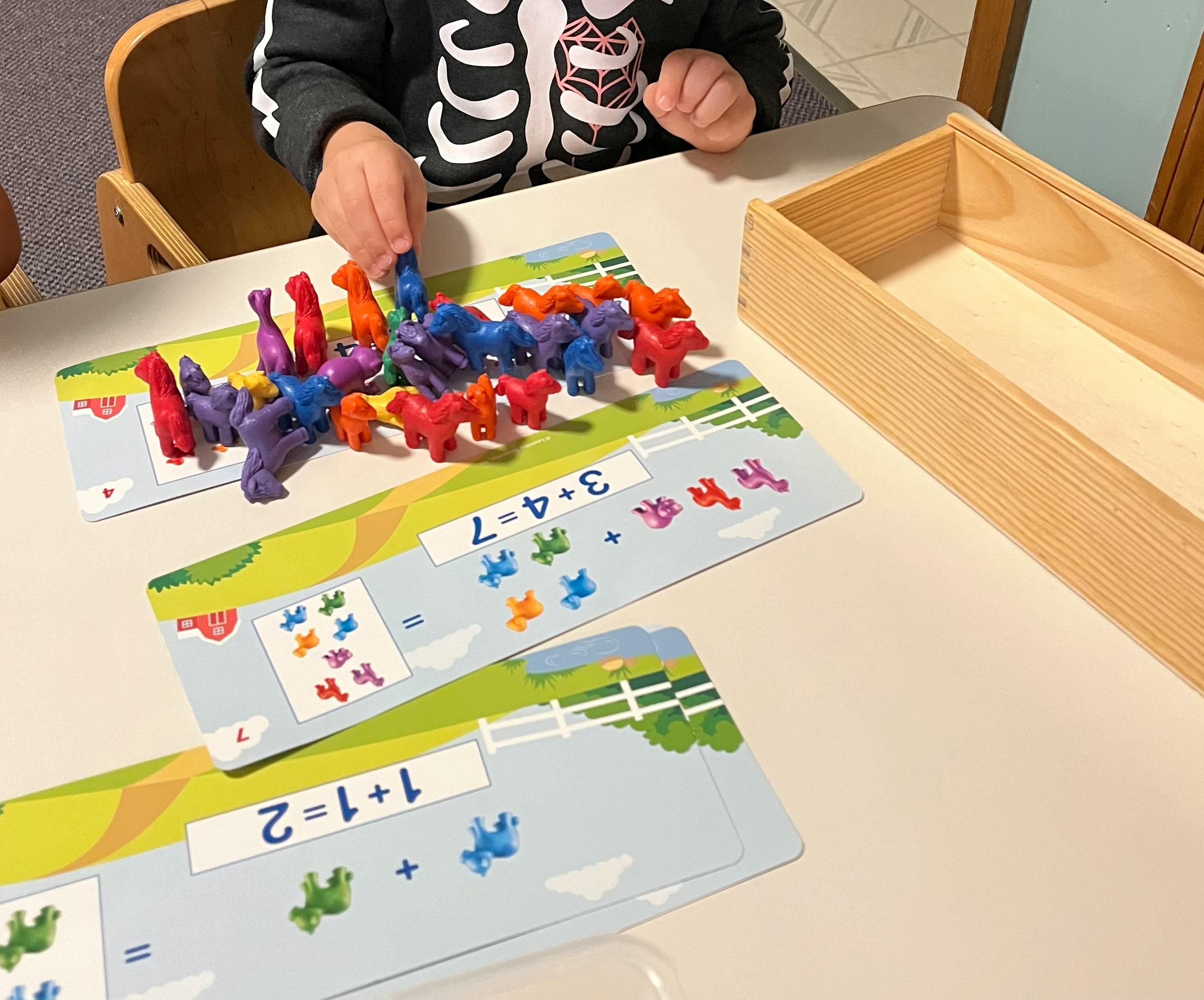 Child's hands arranging colorful animal counters on math activity cards