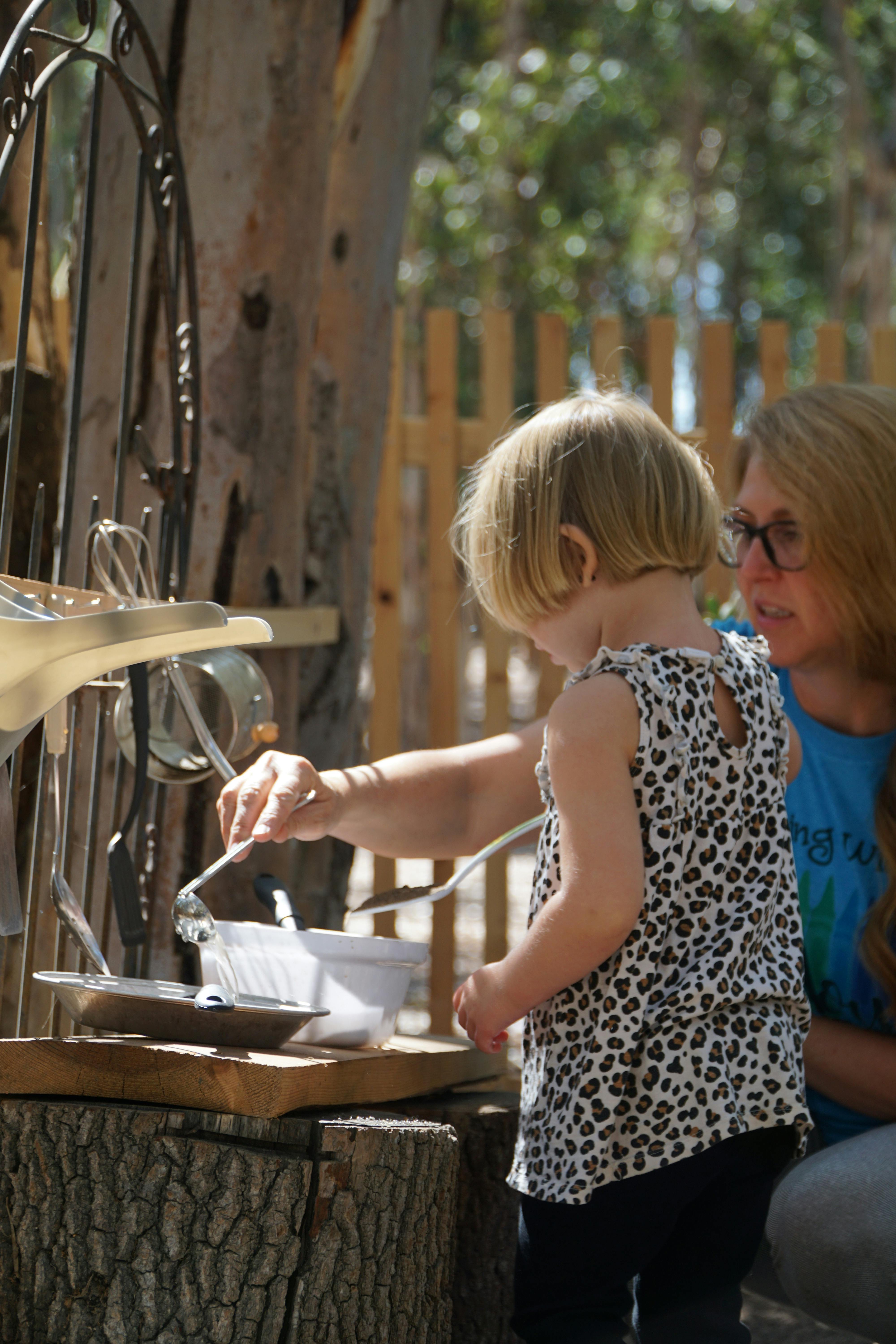 Child and person playing with kitchen utensils outdoors