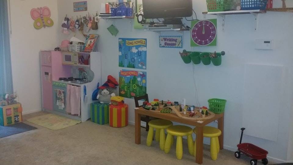 Playroom with toy kitchen, table with train set, and small stools