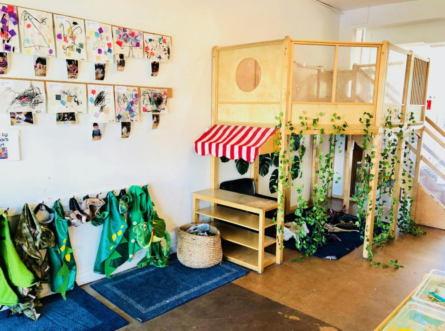 Playroom with a wooden play structure, a small market stall, and children's artwork