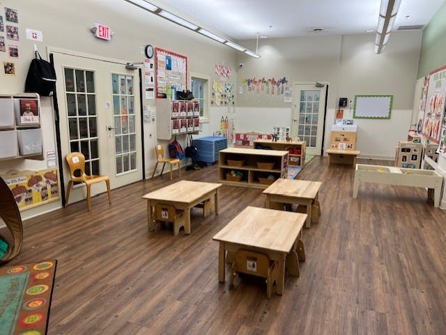Empty classroom with small wooden tables and chairs, artwork on walls