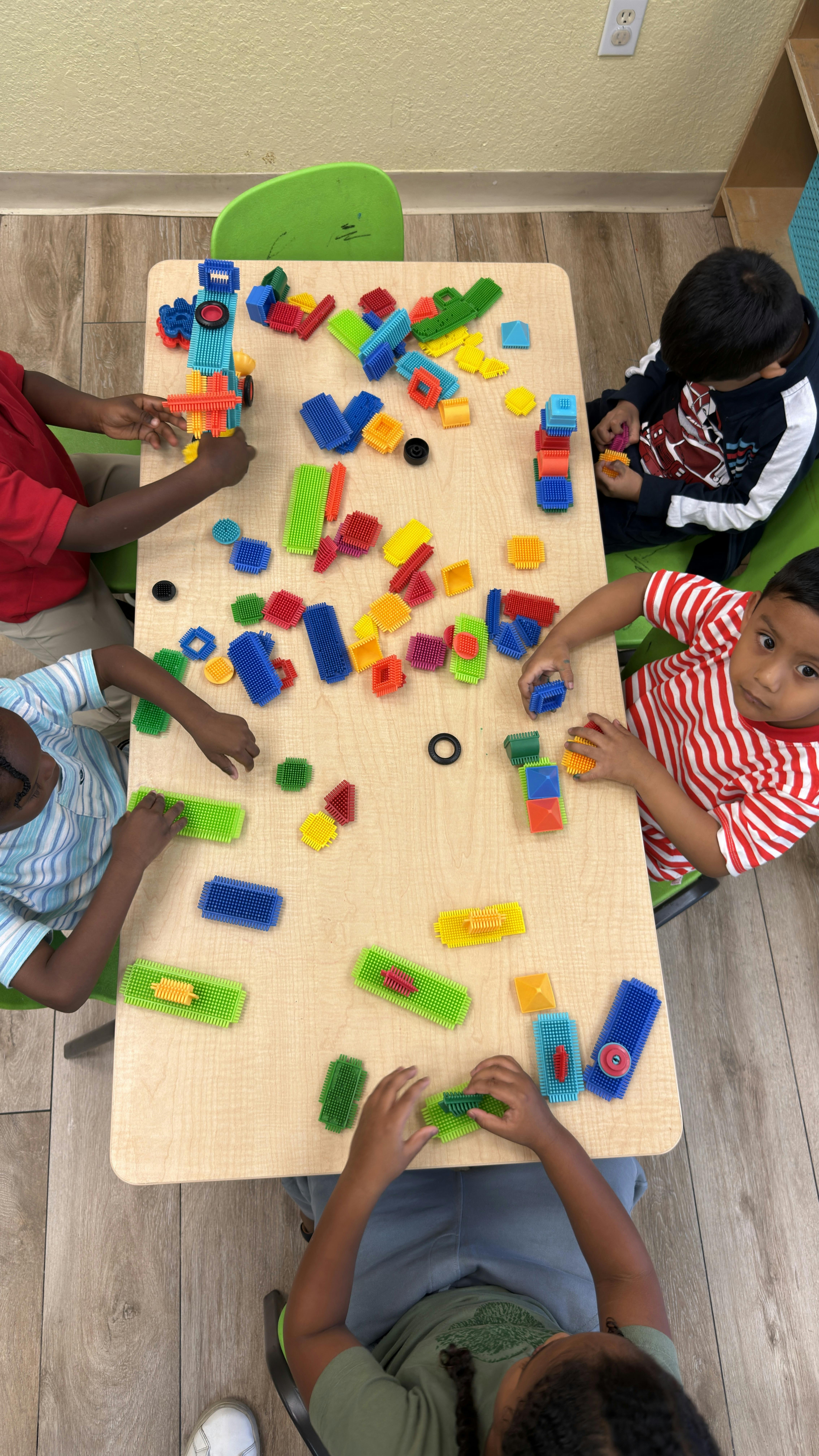 Children sitting at a table building with plastic construction blocks