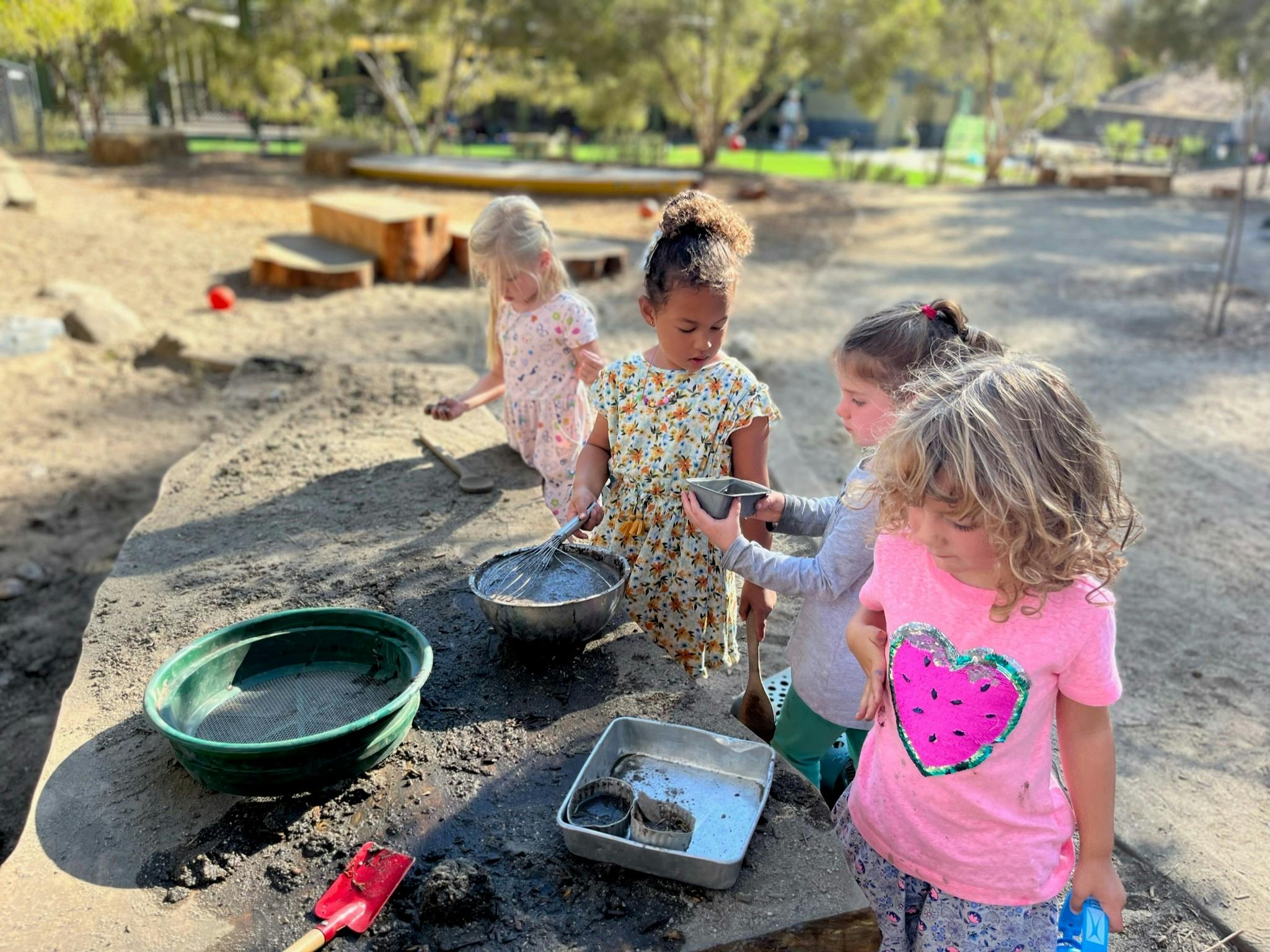 Four children playing with bowls and sand outdoors