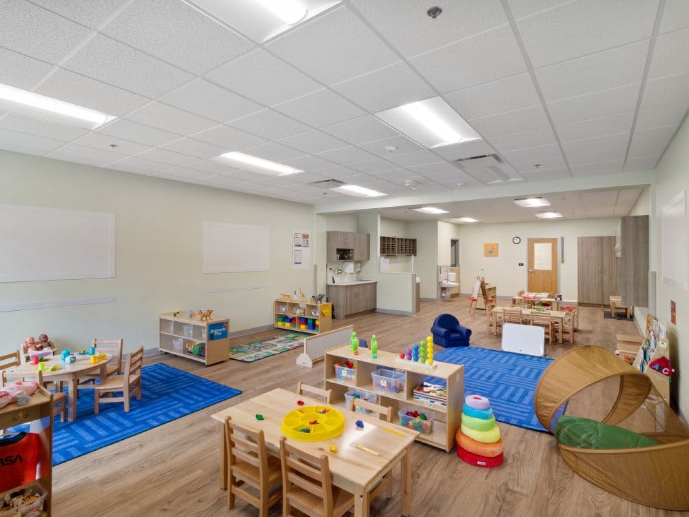 An empty early childhood education classroom with small tables, chairs, and play areas