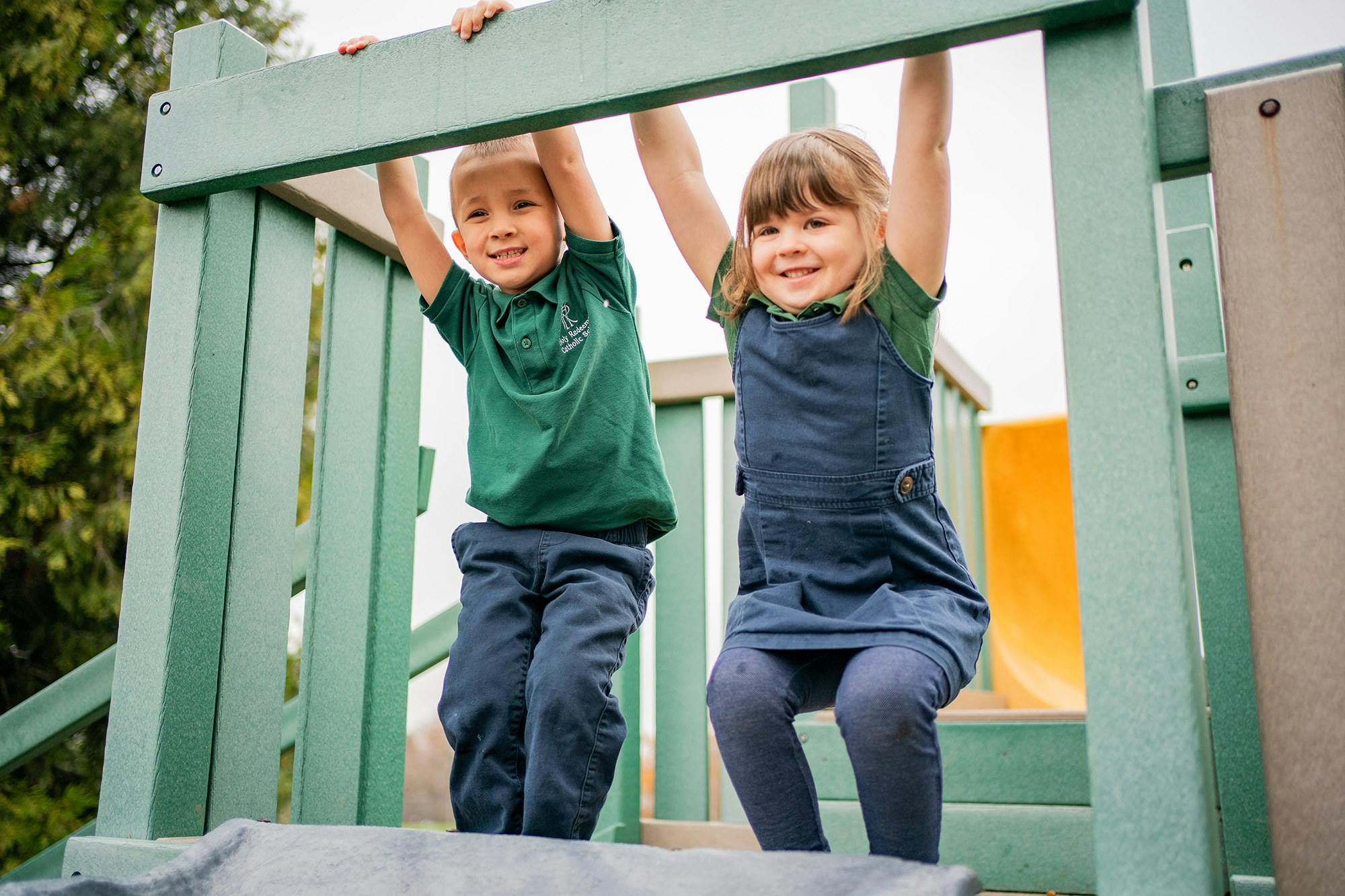Two children hanging from a green play structure