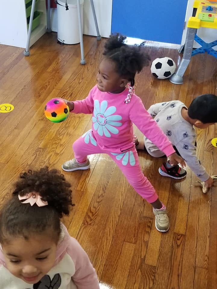 Child in pink outfit holding a colorful ball, another child on the floor