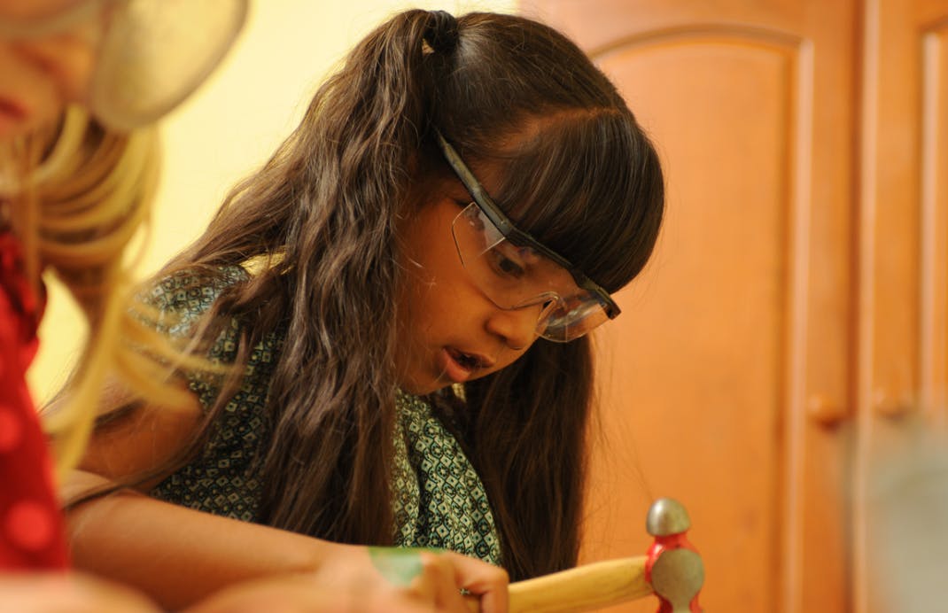 Child wearing safety glasses and holding a hammer