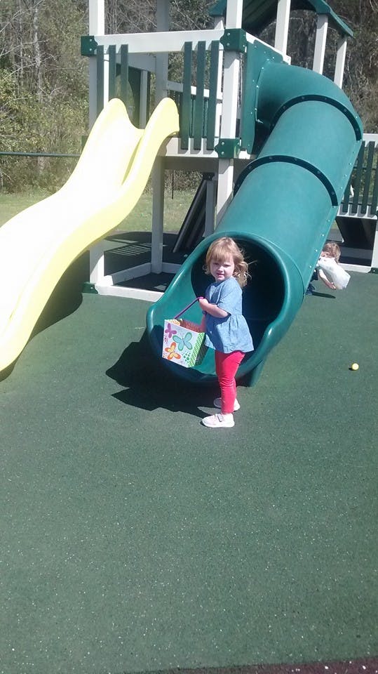 Child standing at the bottom of a playground slide holding a basket