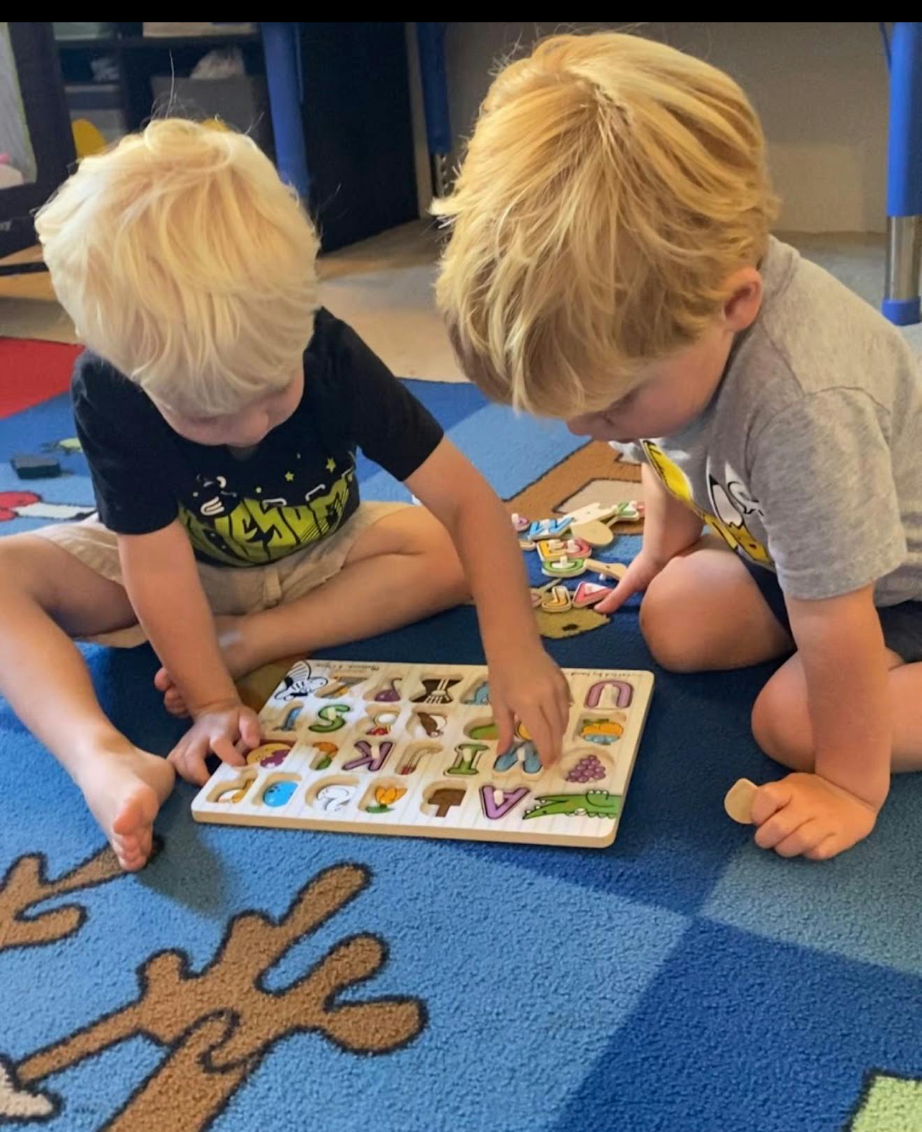 Two children sitting on a rug playing with an alphabet puzzle