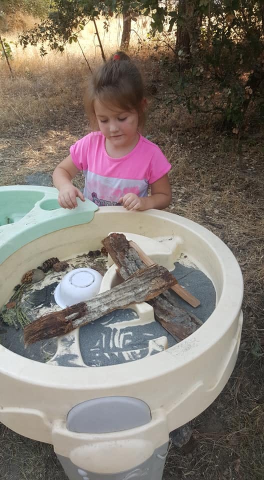 Child playing with a water table filled with sticks and a bowl