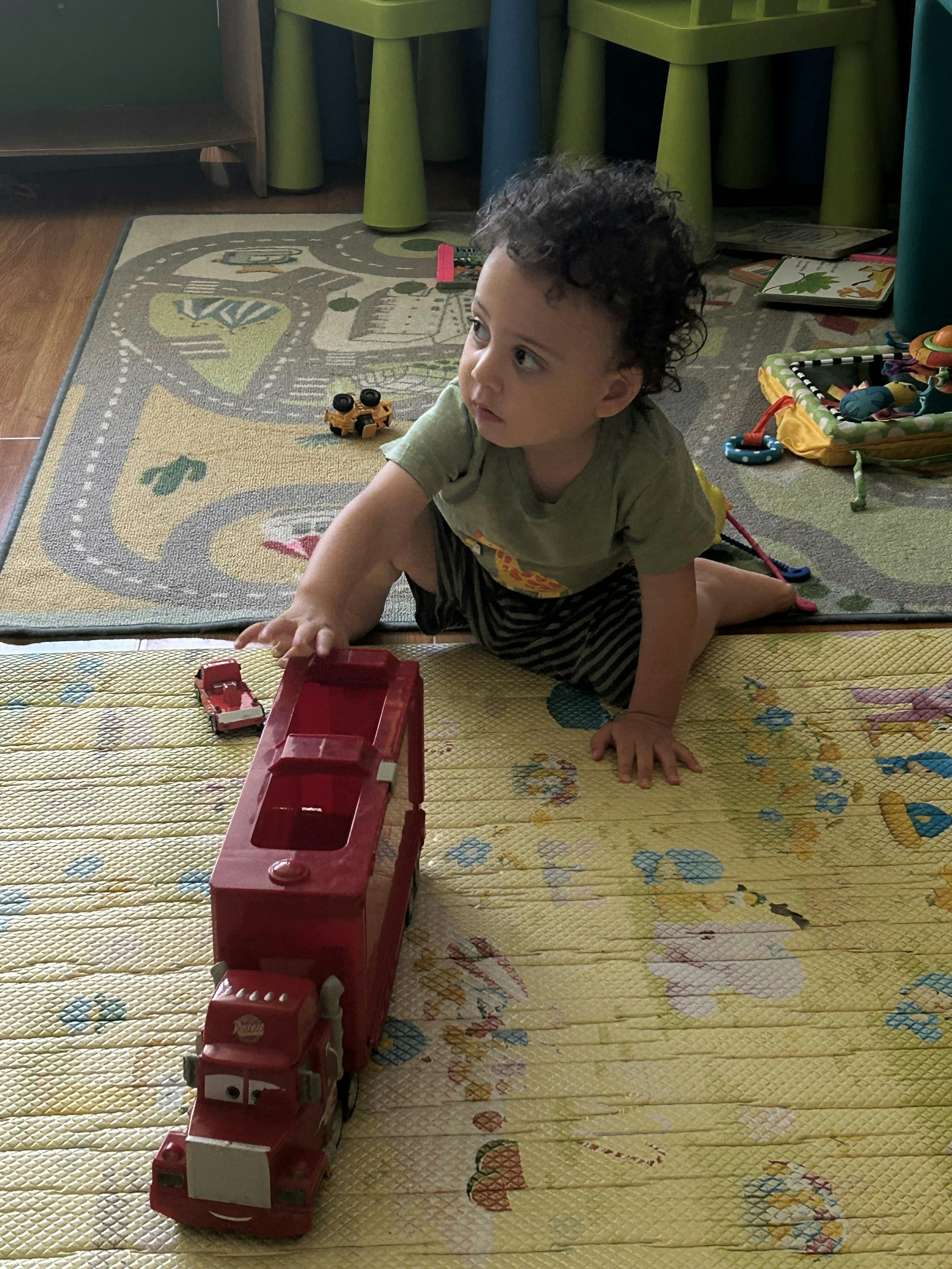 Child on hands and knees reaching for a red toy truck