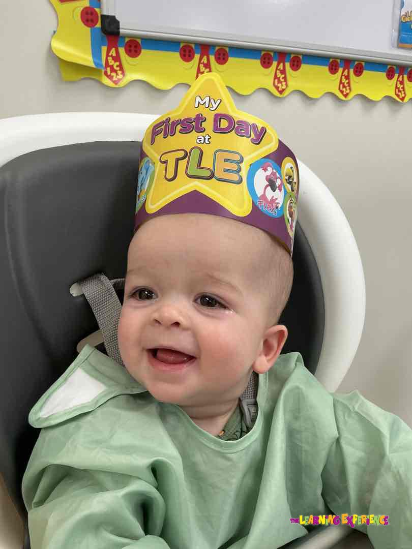 Smiling baby wearing a crown that says "My First Day at TLE"