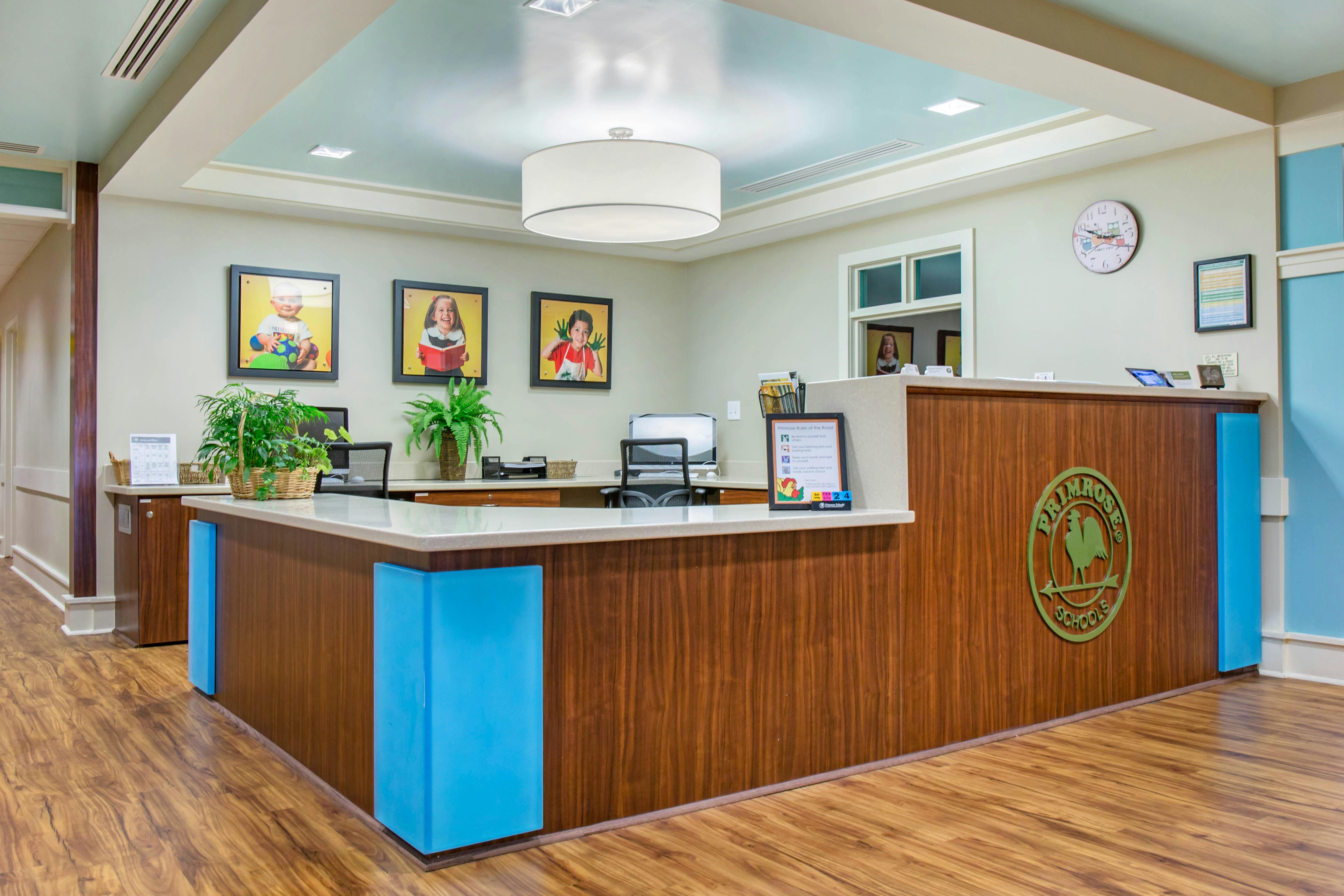 Reception desk with a “Primrose Schools” logo, three framed child portraits, and plants