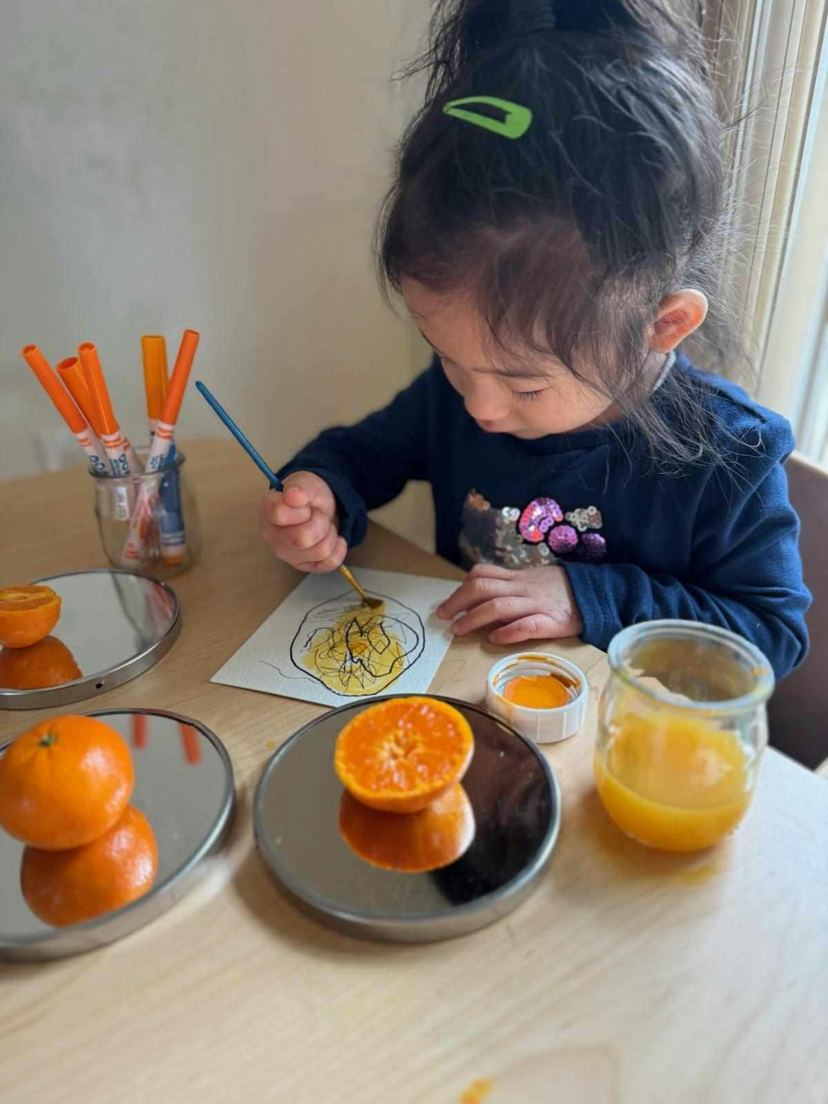 Child painting a picture of an orange with orange paint