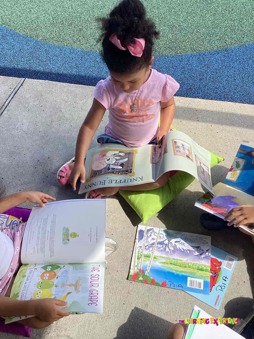 Child reading a book about "Knuffle Bunny" on a green cushion outdoors