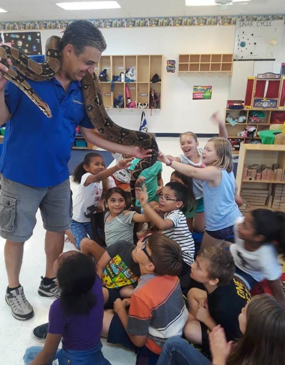 Person holding a snake with children gathered around in a classroom