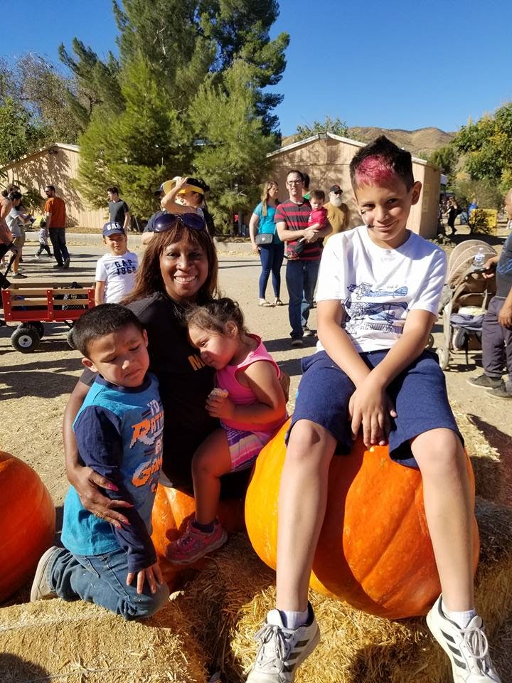 Person with two children, one child sitting on a pumpkin