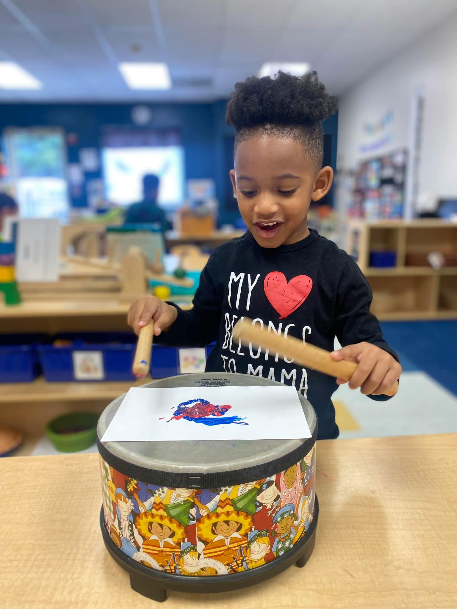 Child playing with drumsticks on a drum with paper and paint