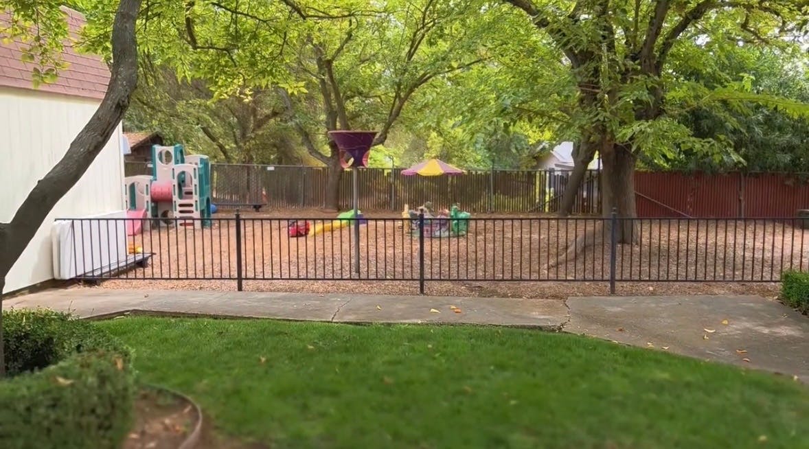 Playground with climbing equipment and toys inside a fenced outdoor area