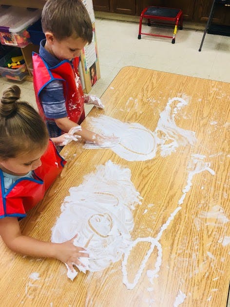Two children in aprons playing with white foam on a table