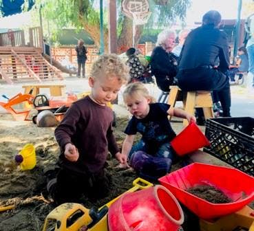Two children playing in a sandbox with toys