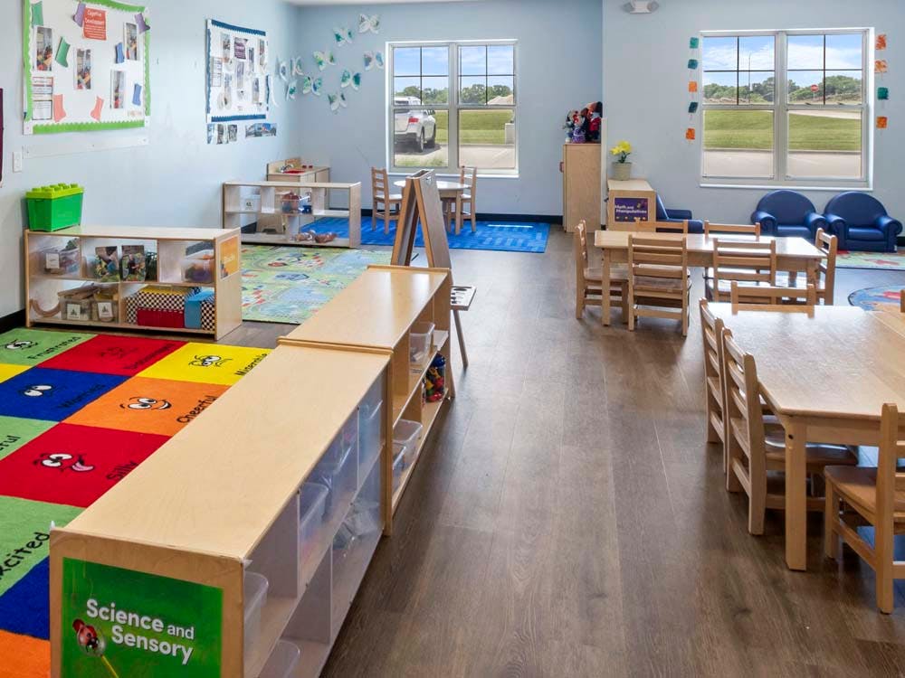 Classroom with tables, chairs, colorful rugs, and shelves filled with learning materials