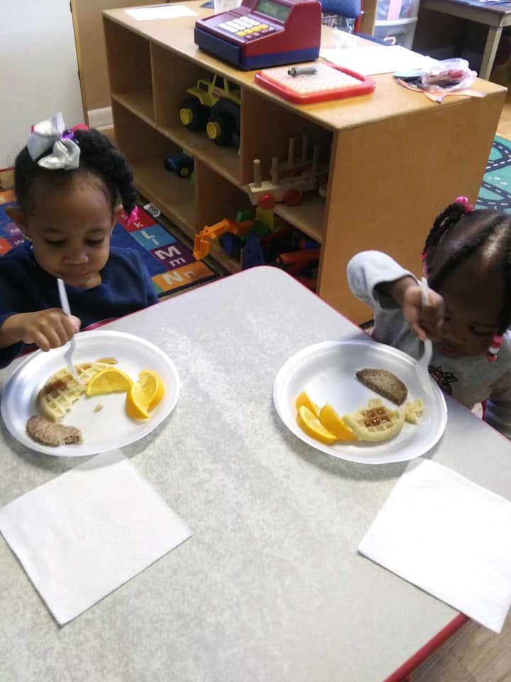Two children eating at a table in a classroom