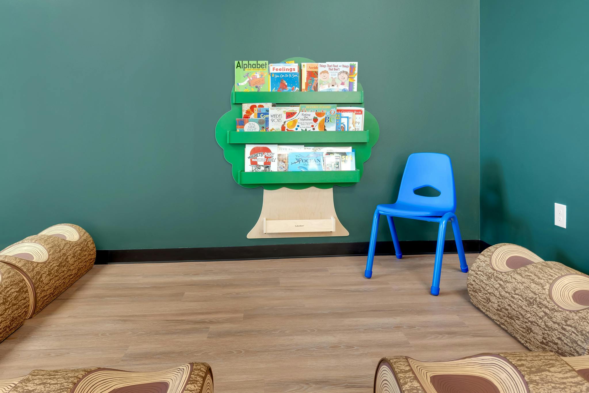 Tree-shaped bookshelf with books and a blue chair in a room