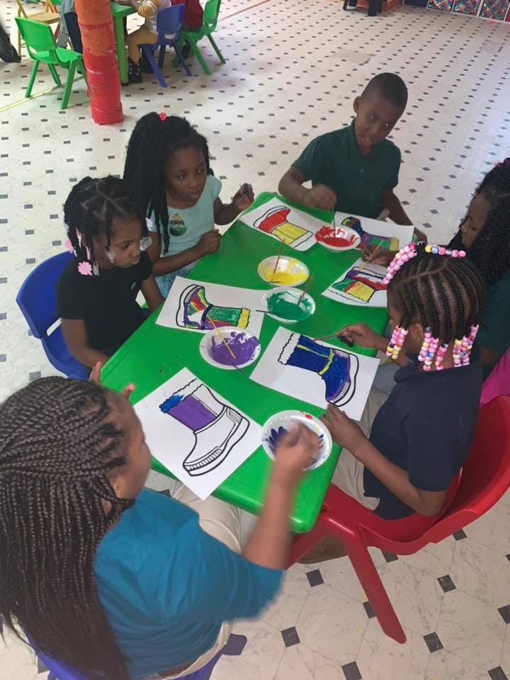 Children painting shoe outlines at a green table