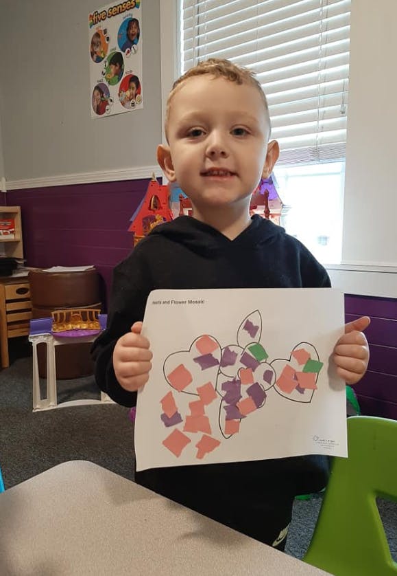 Child holding up a paper with heart shapes filled with colorful paper pieces