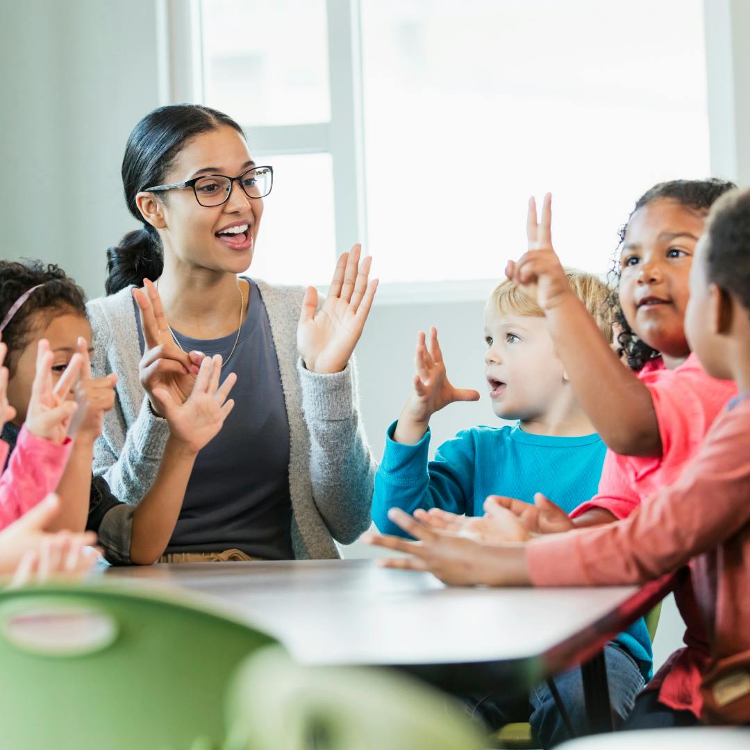 Adult and children raising hands in a classroom