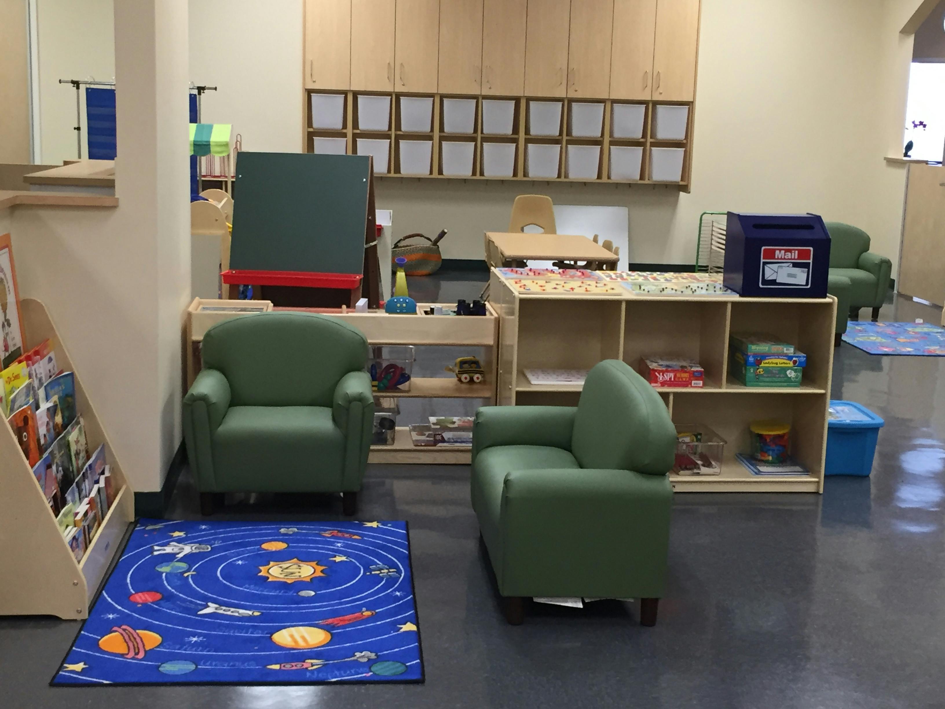 Classroom with green chairs, a blue rug, and wooden shelves
