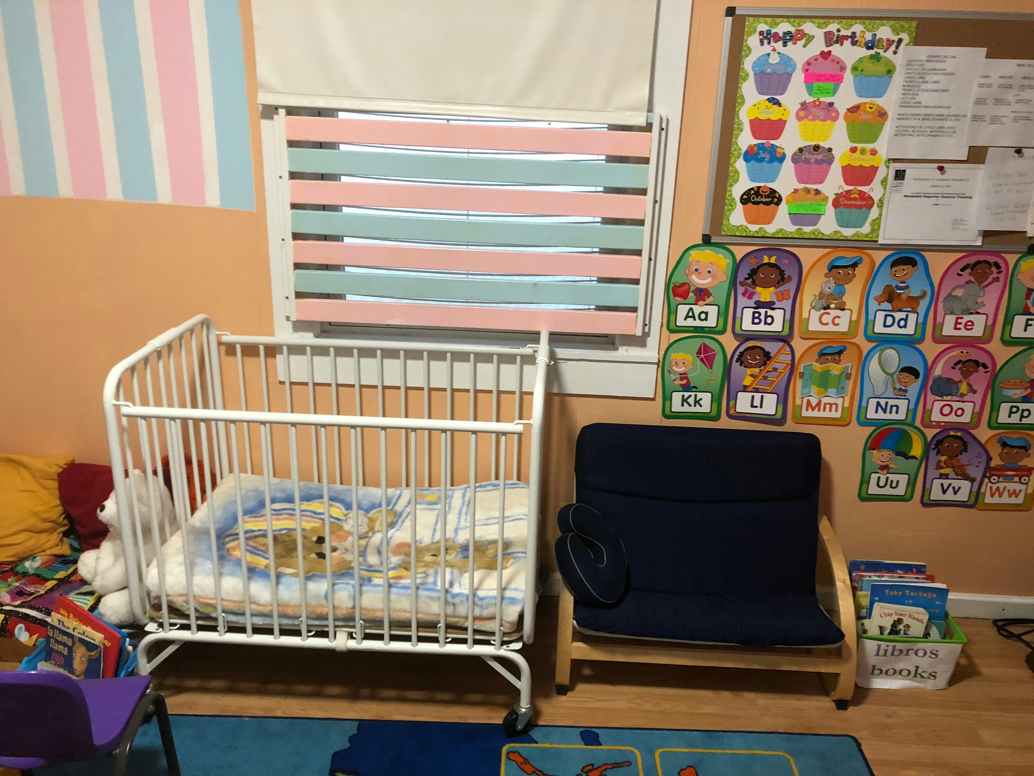 White crib with bedding next to a blue chair in a room with decorations