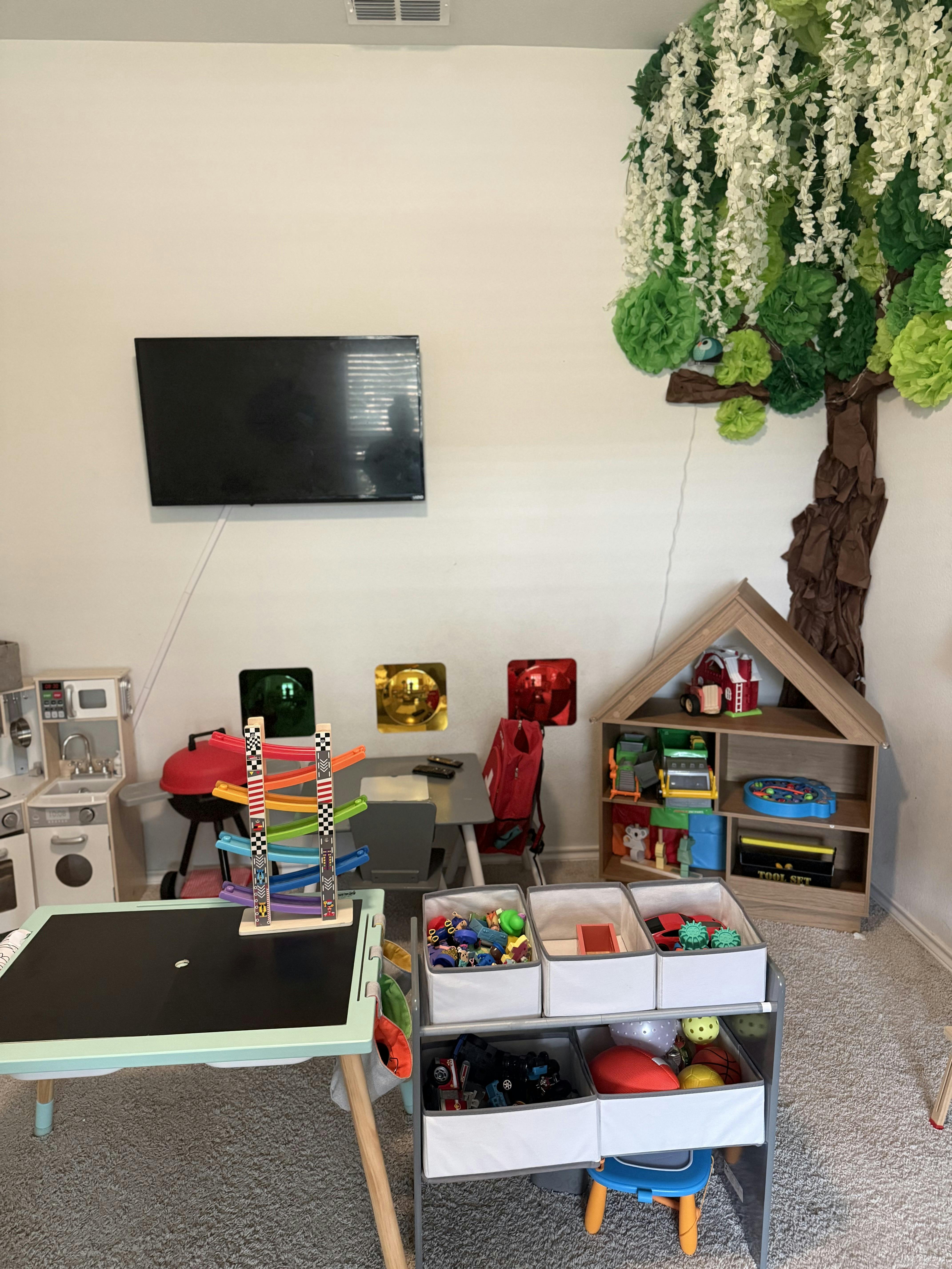 children's play area with toys, a mini kitchen, and a tree mural