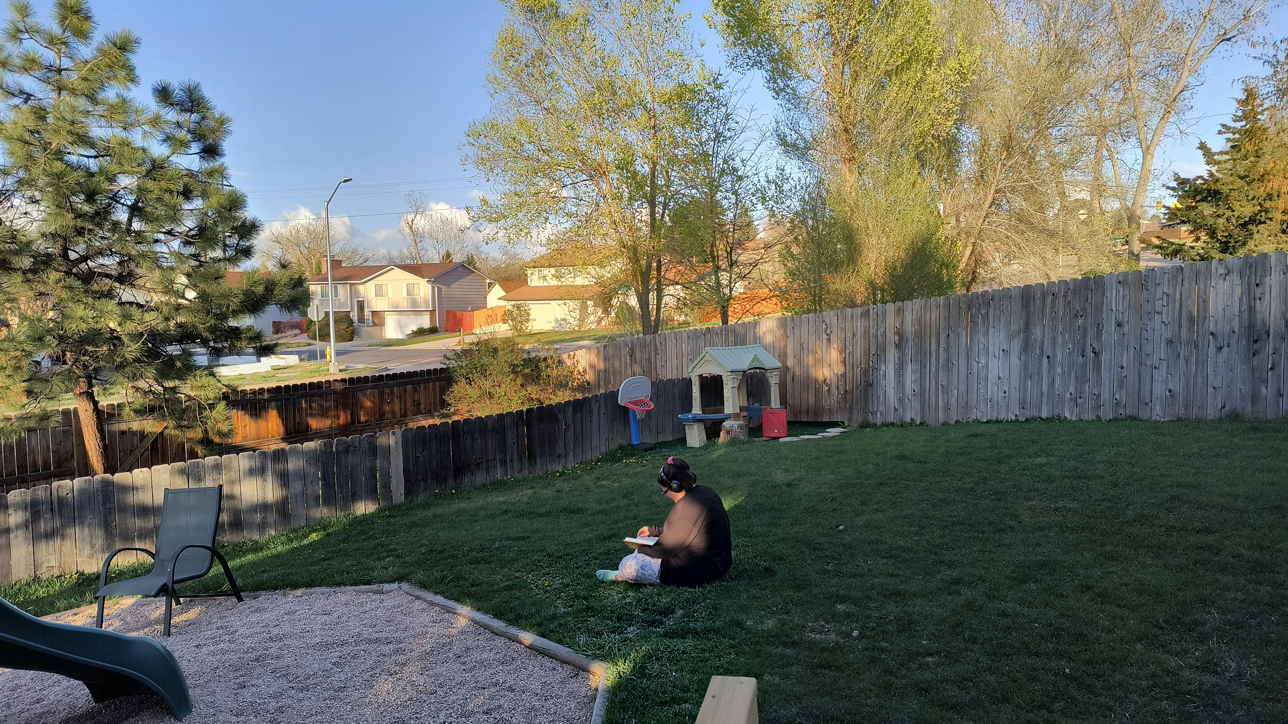 Person wearing headphones sitting on the grass reading a book