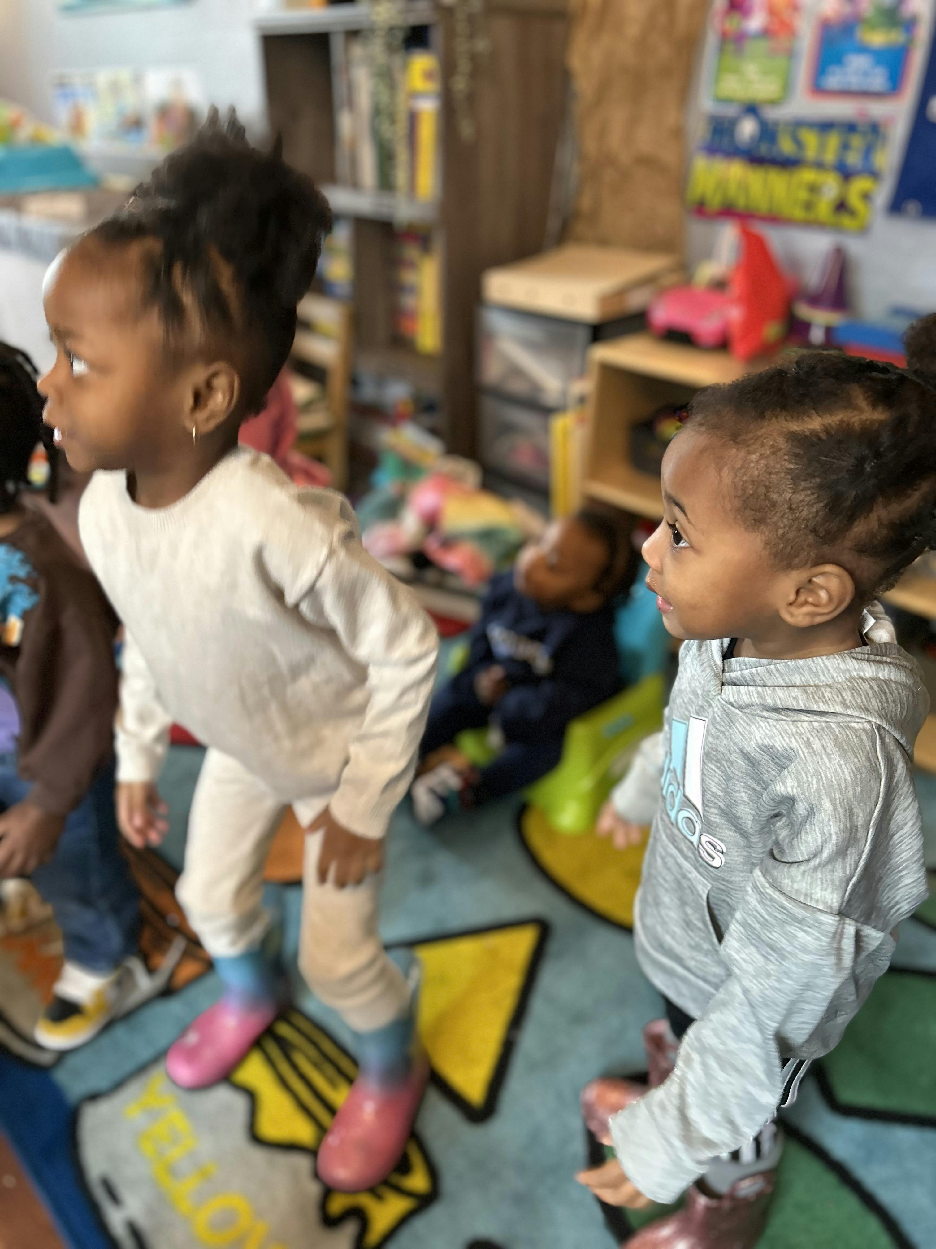 Three children standing and sitting in a classroom