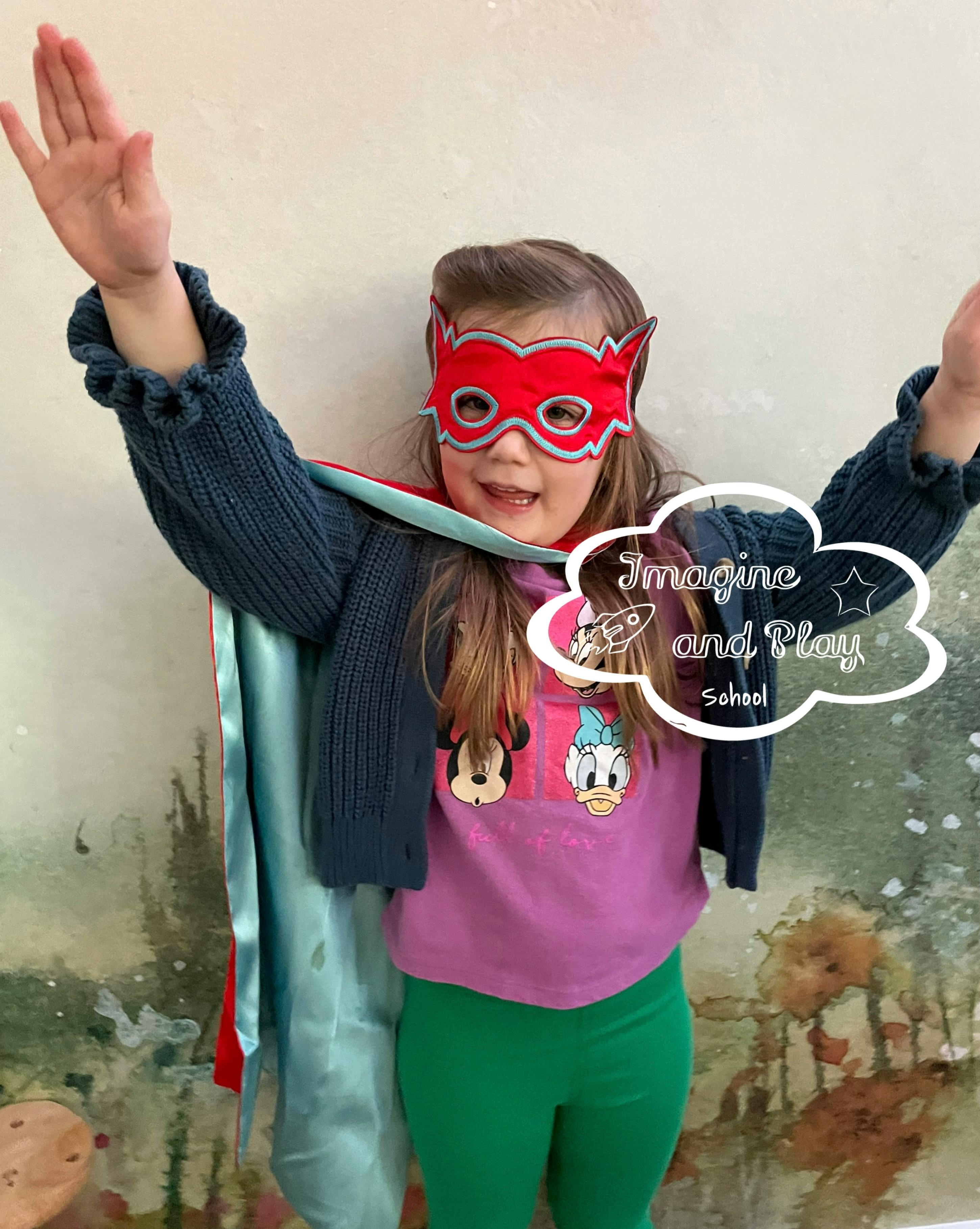 Child wearing a superhero mask and cape, arms raised in the air
