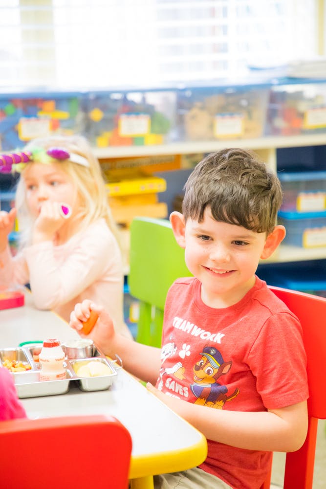 Child in red shirt holding food at a table with another child