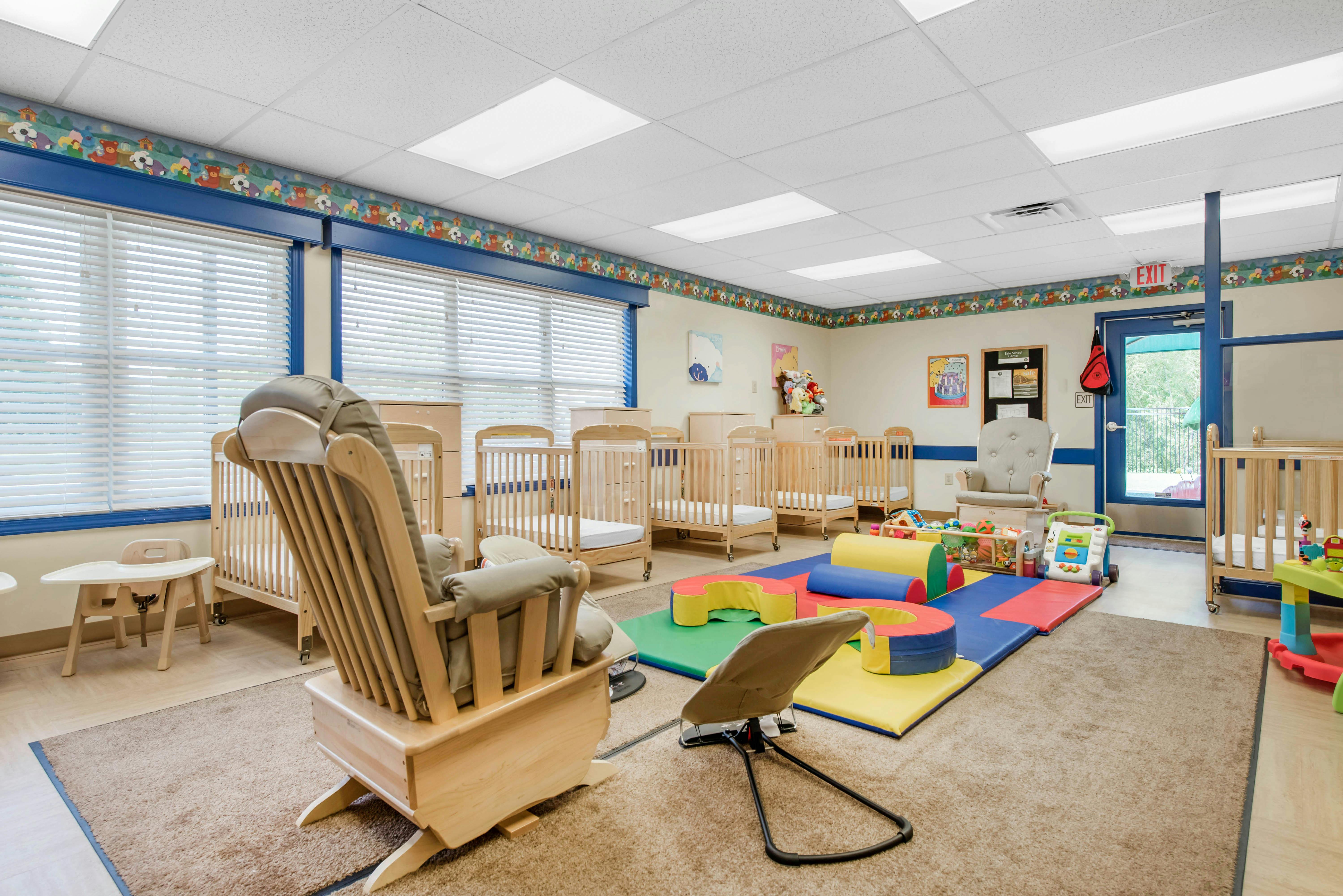 A nursery room with multiple cribs, a rocking chair, and play mats with colorful soft blocks