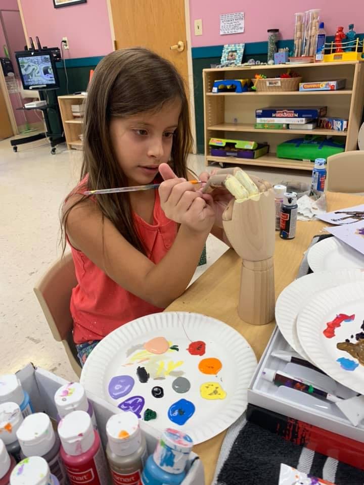 Child painting a wooden hand model