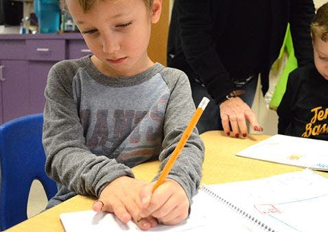Child writing with a pencil at a desk