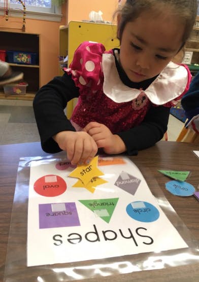 Child placing a yellow star shape on a paper with the word "shapes"